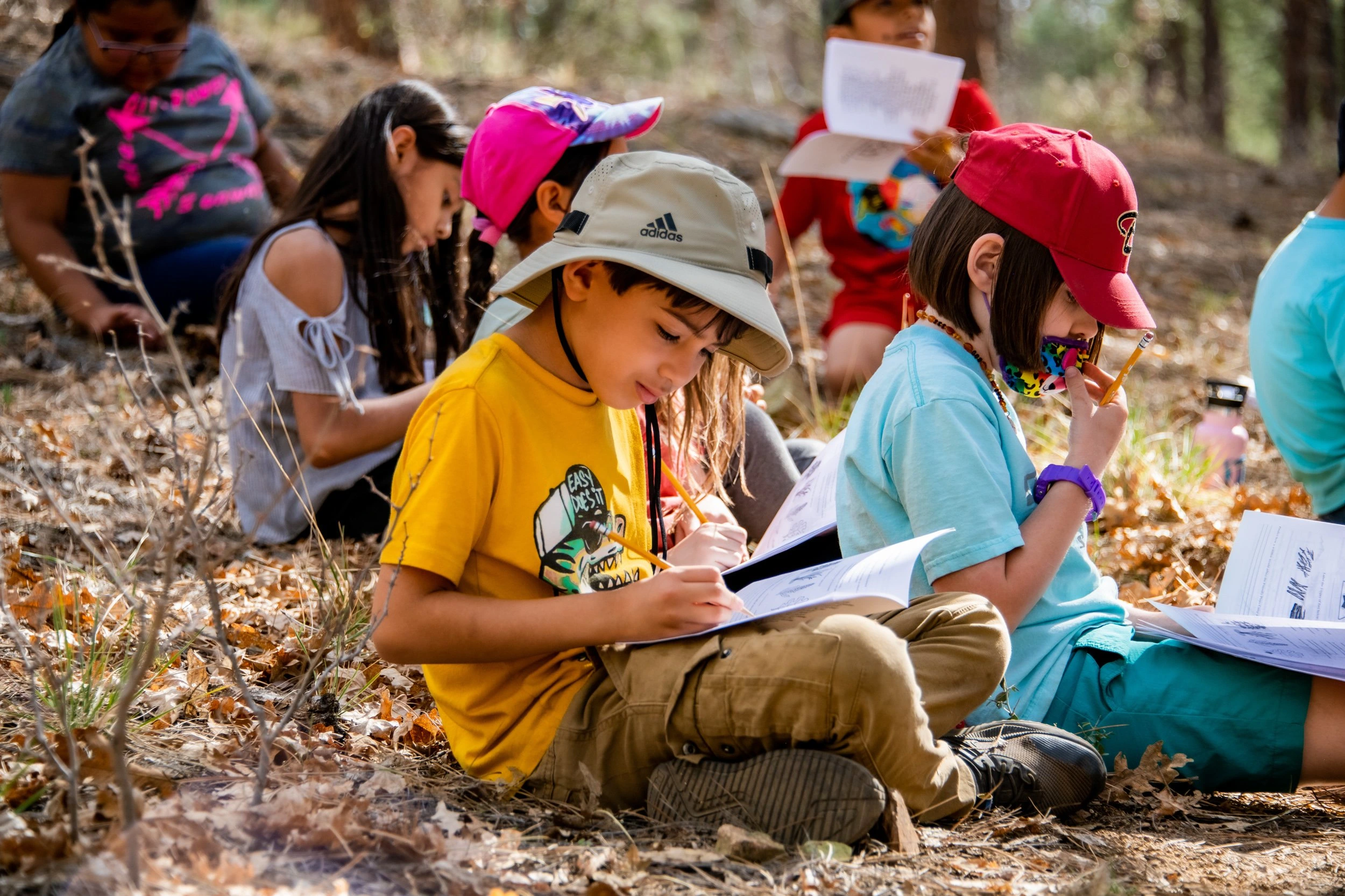 a group of children sitting on the ground writing on paper