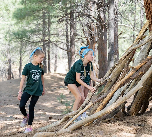 a group of girls in green shirts and blue bandanas climbing up a teepee